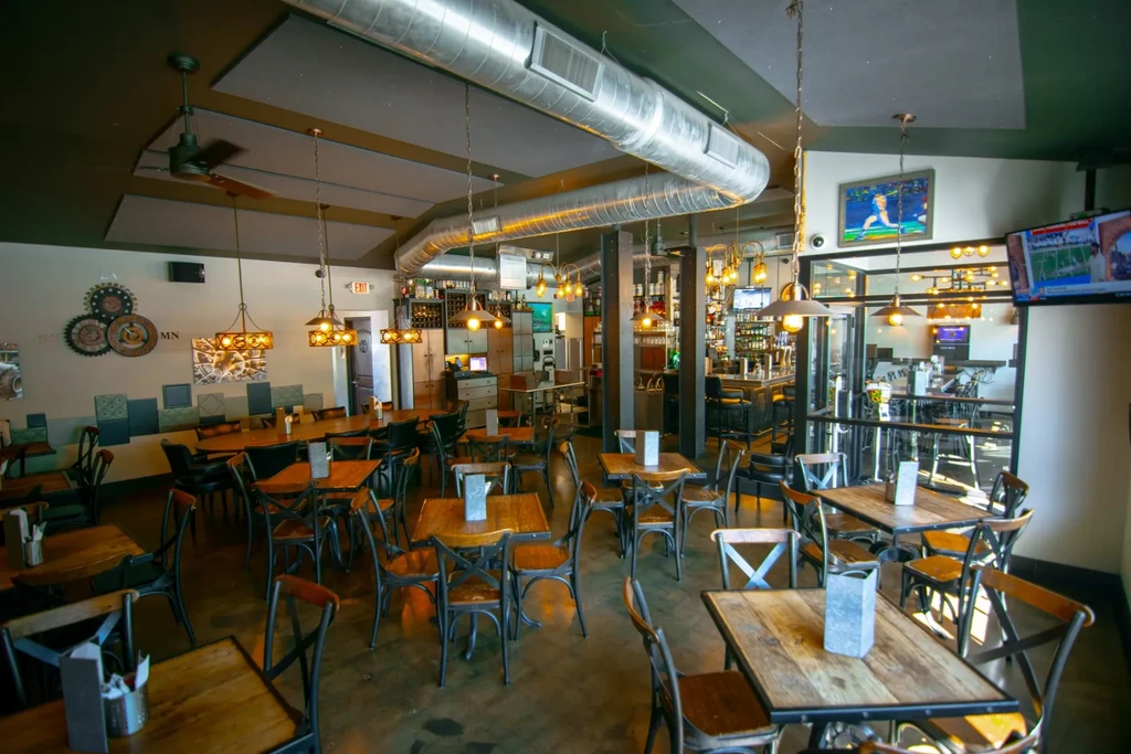Industrial-chic restaurant interior with tables, a bar, and exposed ductwork.