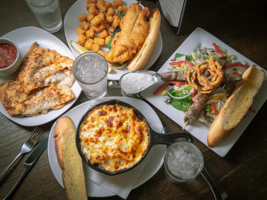 Overhead view of various restaurant meals and drinks on a dark table.
