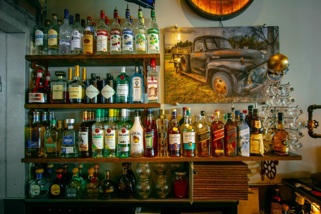 Four wooden shelves filled with liquor bottles, glasses, and rustic decor.