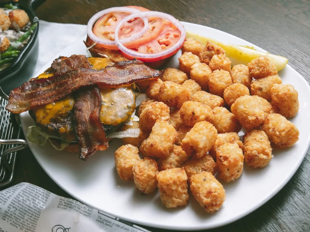 Overhead: Open-faced cheeseburger with bacon, tater tots, and a pickle spear.