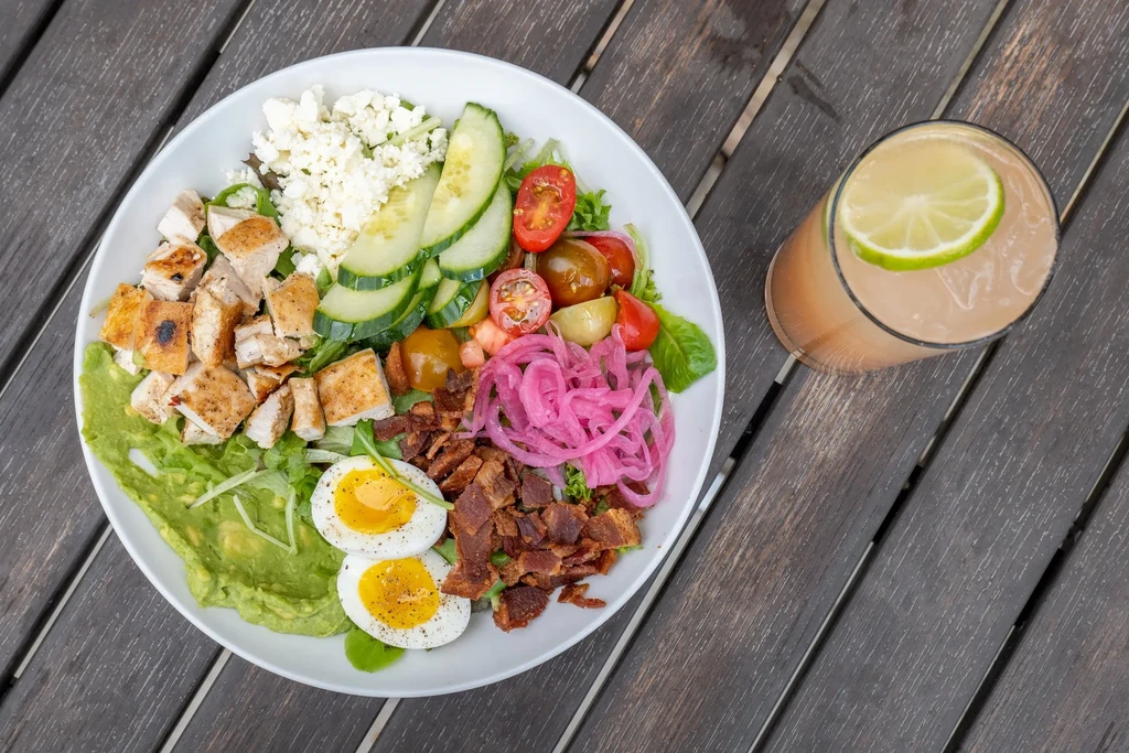 Colorful salad bowl with grilled chicken, eggs, avocado, and pickled onions.