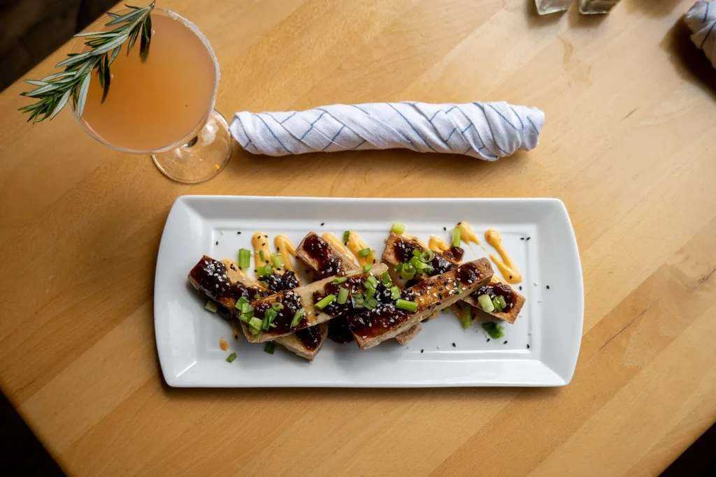 Crispy appetizer, orange cocktail with rosemary, and napkin on wood.