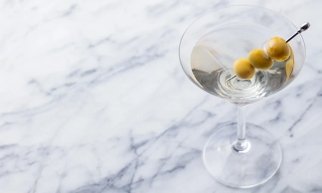 Clear martini with three green olives on a skewer, from above.