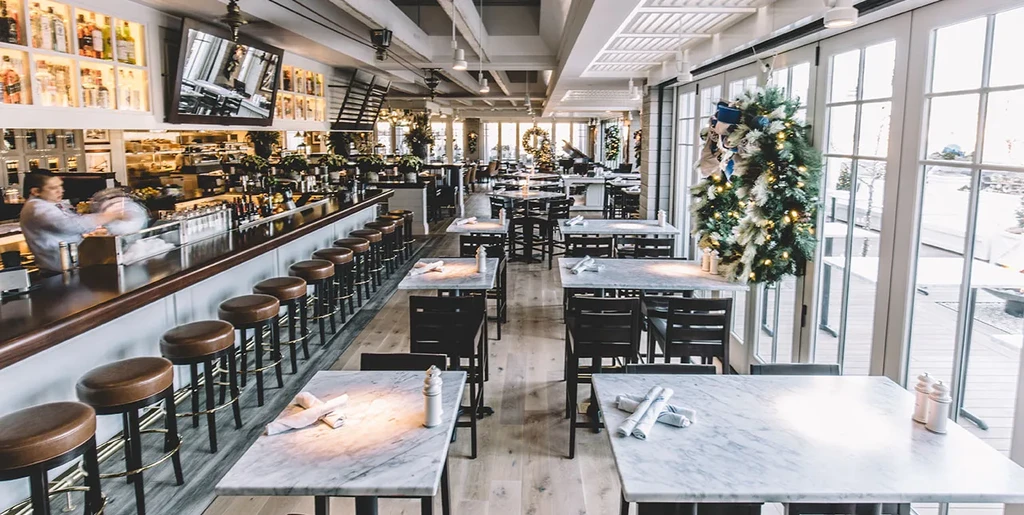 Bright bar and restaurant interior with holiday wreaths and a bartender.