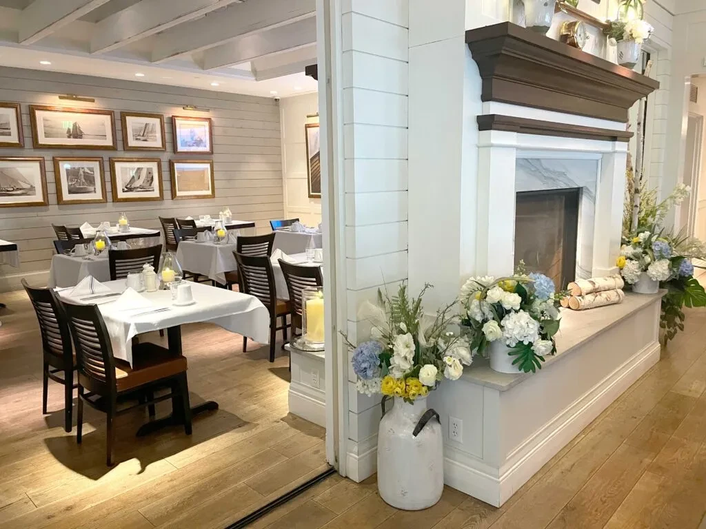 Restaurant interior with set tables, nautical art, and a decorative fireplace.