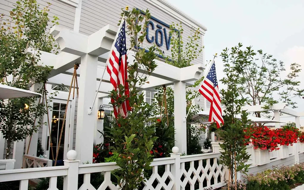 COV restaurant exterior with white pergola, lush greenery, and American flags.