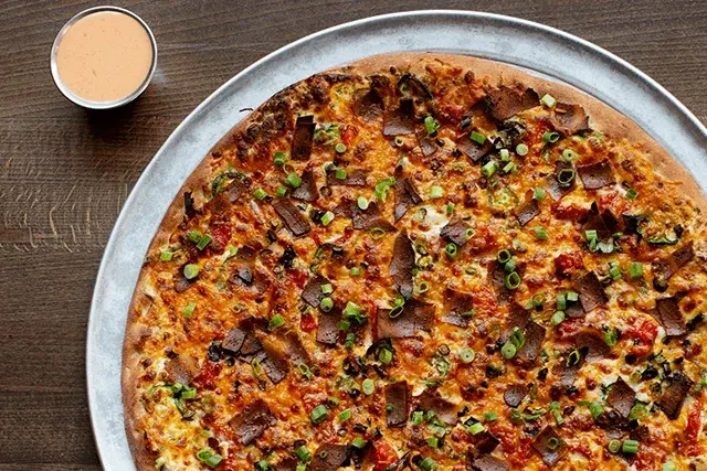 Round pizza with cheese, meat substitute, scallions, and dipping sauce.