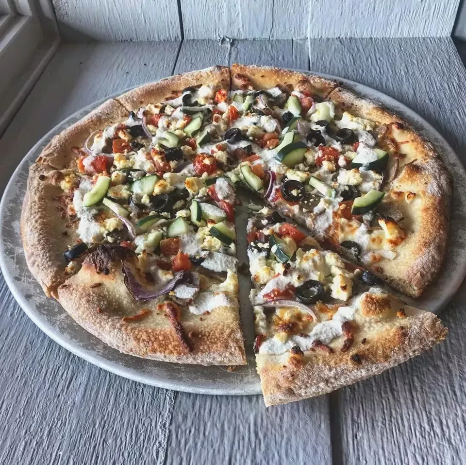 Pizza with feta, olives, tomatoes, cucumber; one slice pulled away.