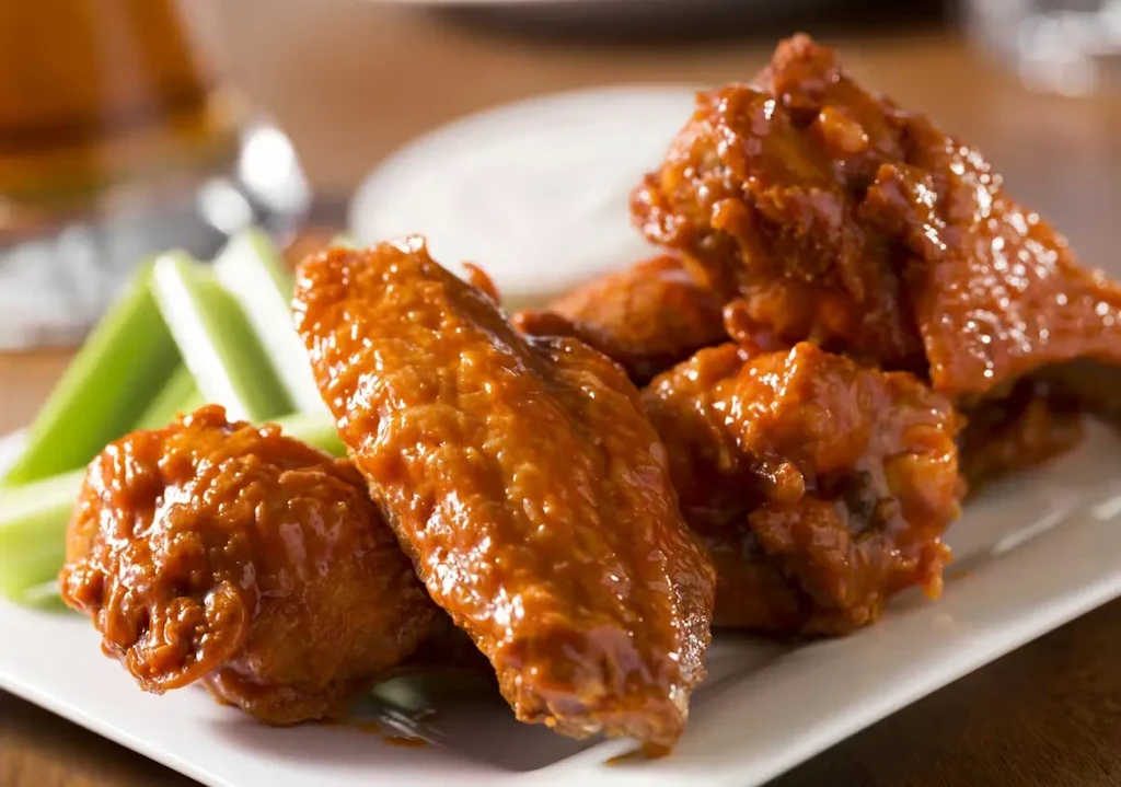Plate of buffalo chicken wings with celery sticks and dipping sauce.