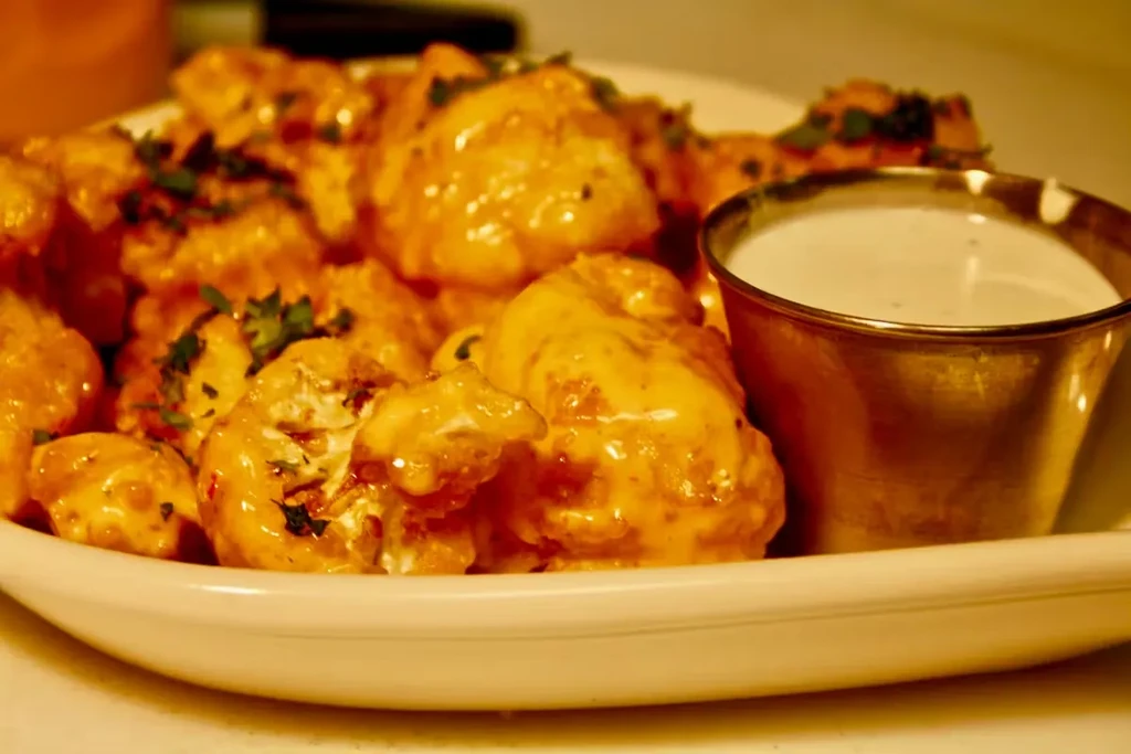 Sauced cauliflower or chicken wings garnished with herbs and a dip.