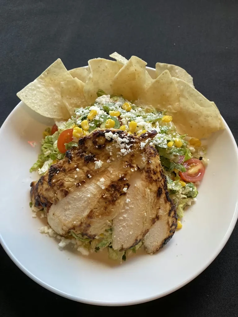 Grilled chicken salad with lettuce, corn, tomatoes, cheese, and tortilla chips.