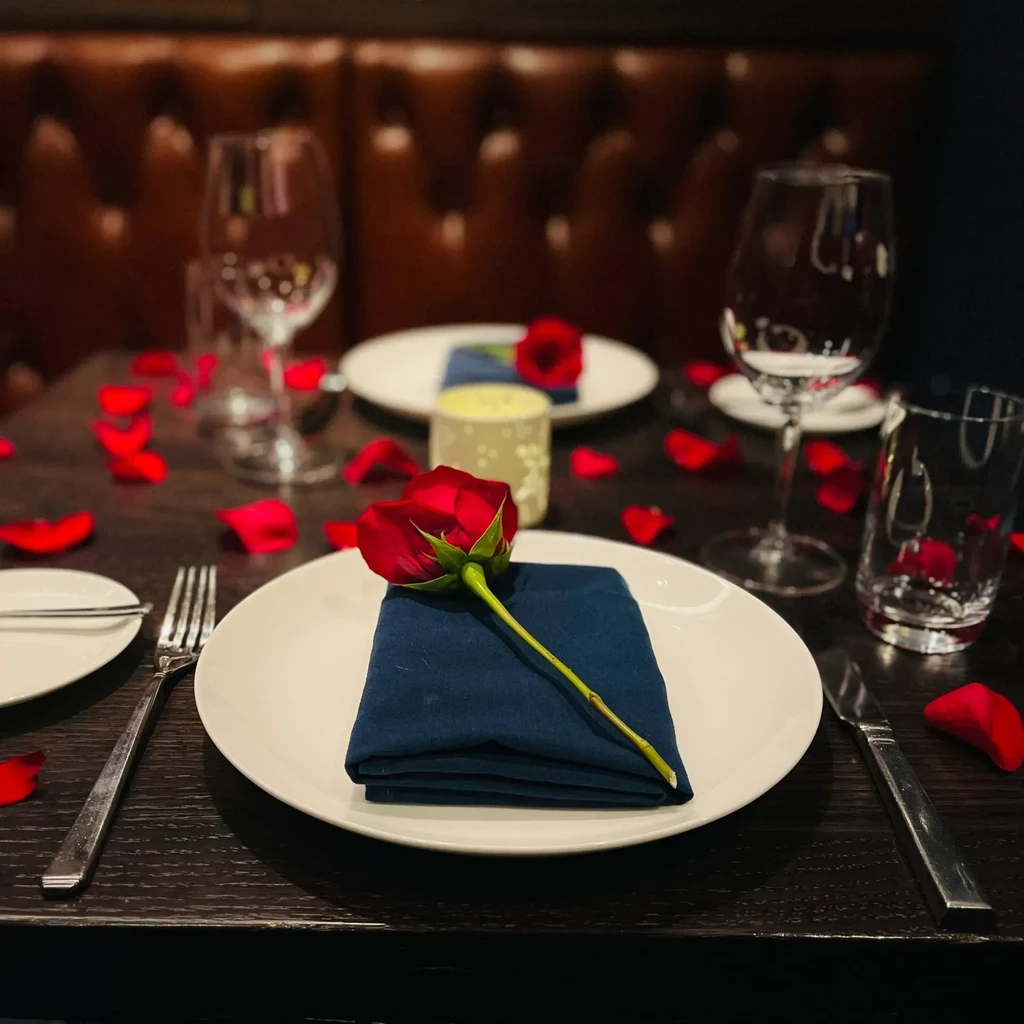 Romantic table setting with white plate, blue napkin, and red rose.