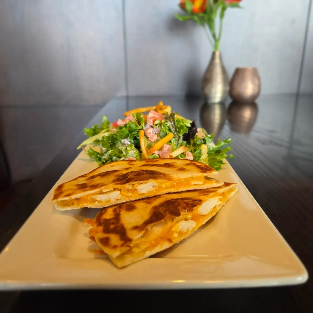 Two grilled chicken quesadilla halves, side salad, and dressing on a plate.