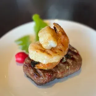 Grilled surf and turf: steak topped with shrimp and radish garnish.