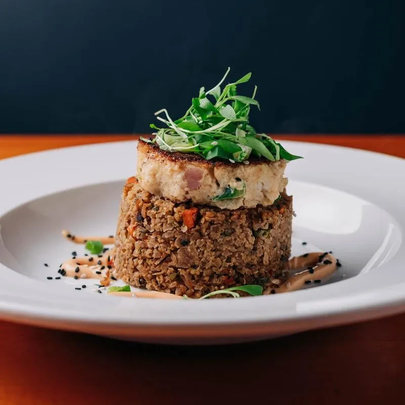 Stacked pan-seared cake on grains, garnished with microgreens and sauce.