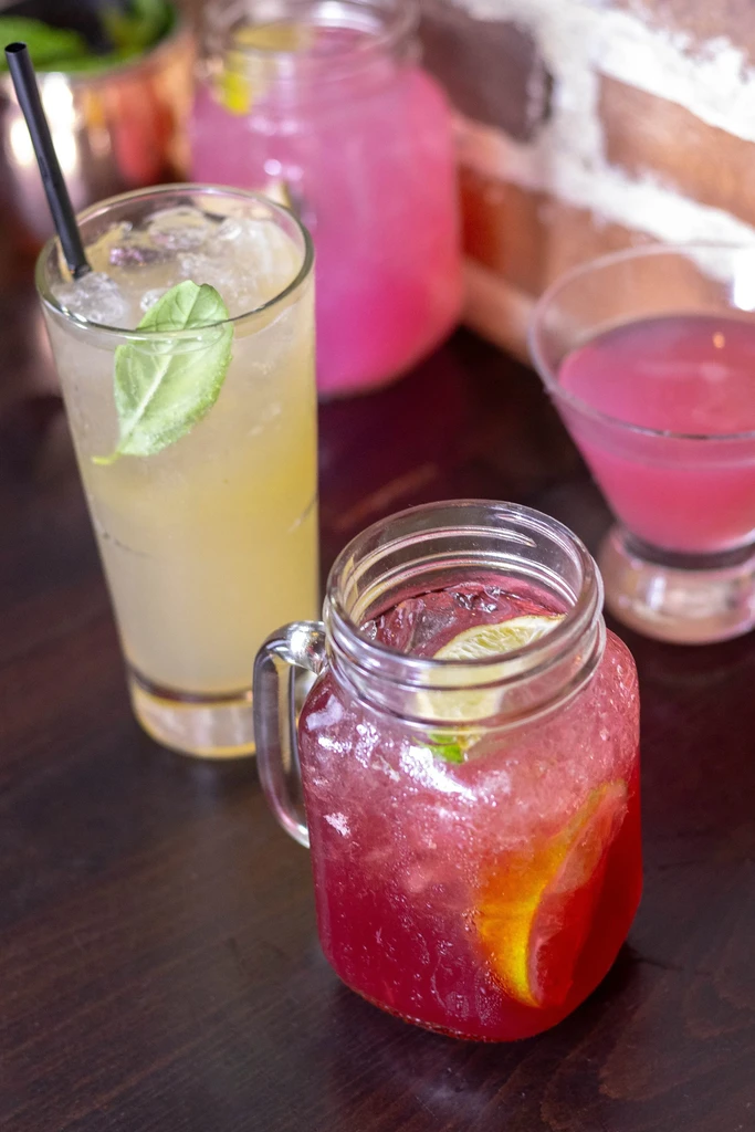 Four colorful drinks with ice and garnishes on a wooden table.