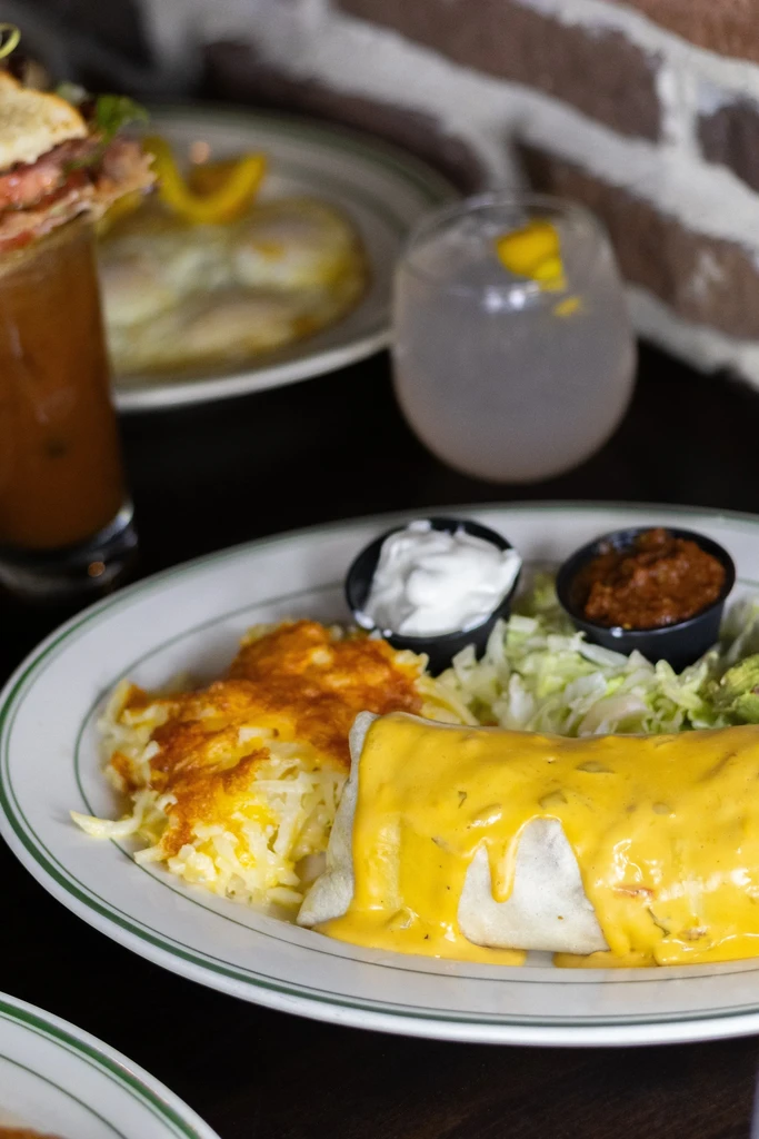Plate with a cheese burrito, hash browns, salsa, and sour cream.