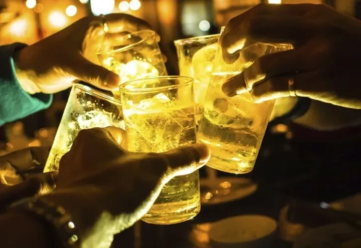Several hands toasting with glasses of amber liquid and ice.