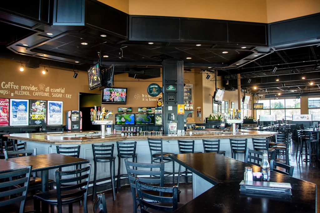Inside a bar with a long wooden counter, stools, and TV screens.