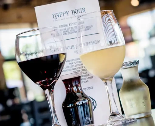 Close-up of red and white wine glasses and a Happy Hour menu.