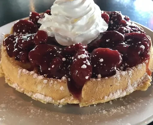 Golden waffle topped with strawberry compote, whipped cream, and powdered sugar.