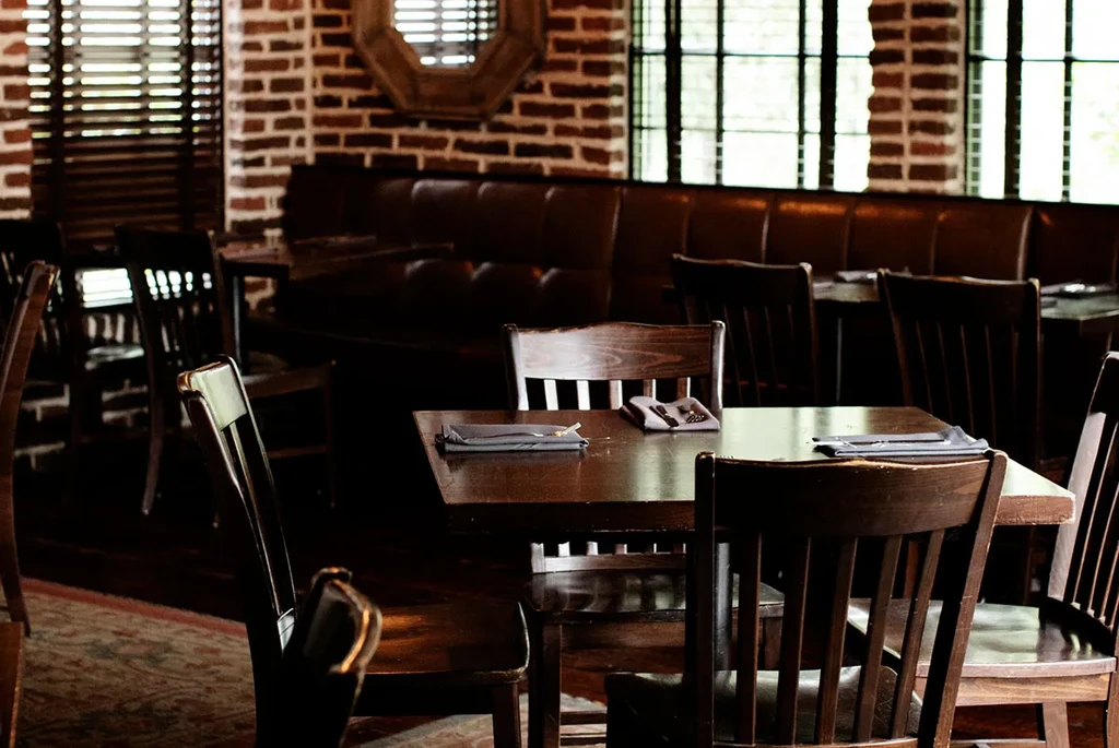 Empty restaurant dining area with wooden tables, leather booths, brick wall.