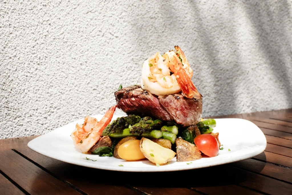 Seared steak and shrimp with roasted vegetables on a white plate.