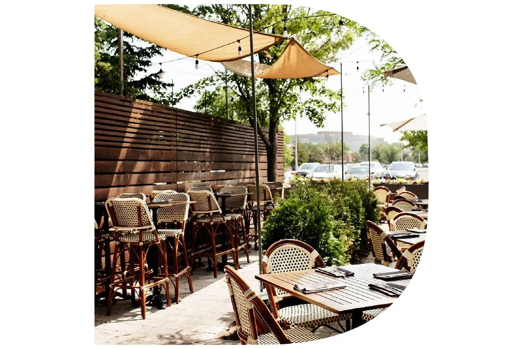 Empty outdoor dining patio with tables, chairs, awnings, and lush greenery.