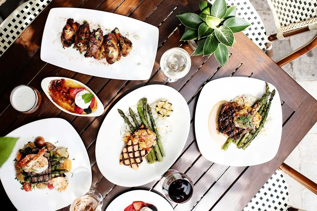 Top-down: Gourmet dishes, wines, beer arranged on an outdoor wooden table.