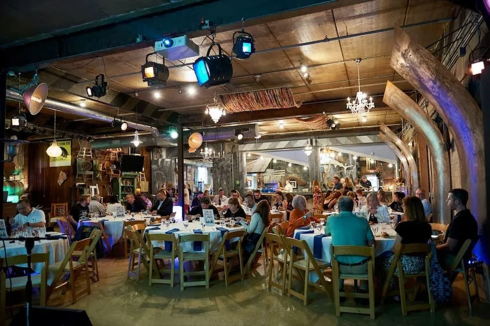 Bustling restaurant interior with industrial ceiling, eclectic lighting, and many diners.