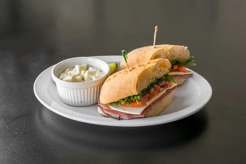 Two deli submarine sandwich halves with potato salad and lime.