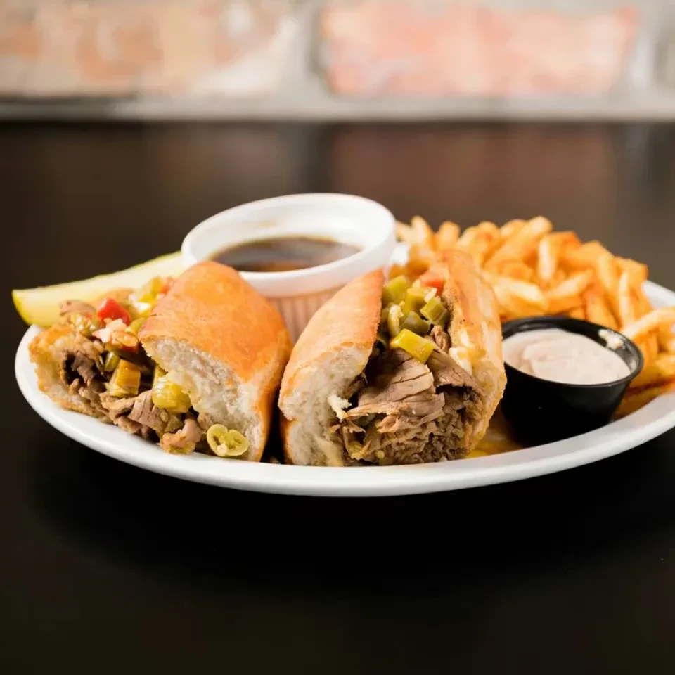 Large meat sandwich, pickled peppers, fries, sauces, and a pickle.