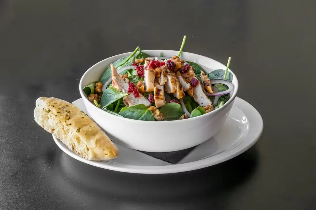 Salad bowl with grilled chicken, spinach, walnuts, cranberries, and bread.