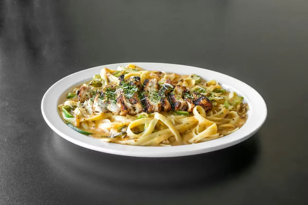 Dish of creamy pasta with grilled chicken, vegetables, herbs, and cheese.
