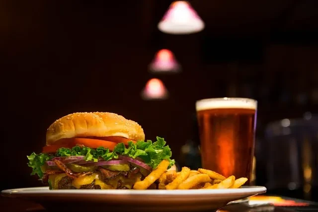 Close-up of a hamburger, fries, and beer in a dark restaurant.