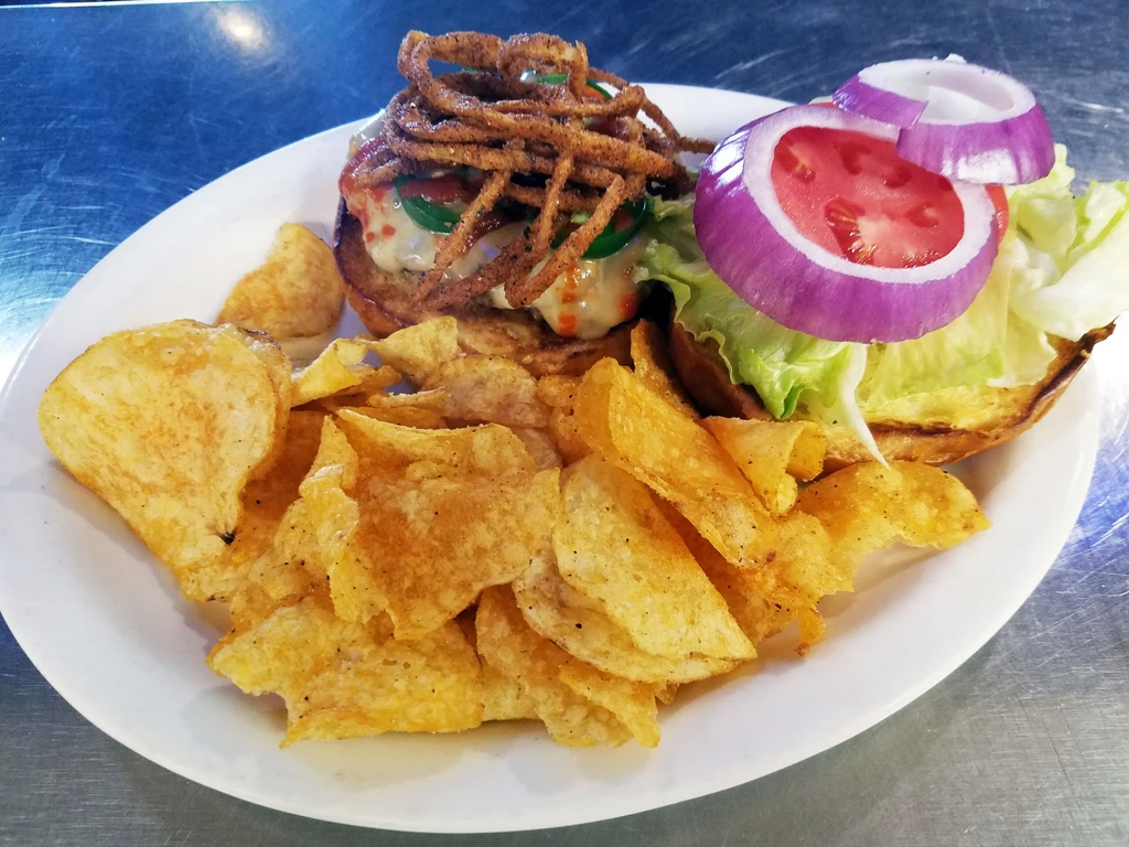 Top-down, open-faced burger with crispy onions, toppings, and potato chips.