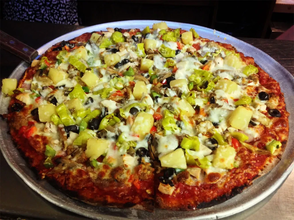 Large, freshly baked pizza with pineapple, olives, peppers, meat, melted cheese.