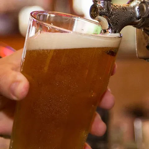 A glass of effervescent golden-brown beer fills from a tap.