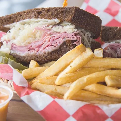 Close-up of a Reuben sandwich, fries, and pickle in a basket.