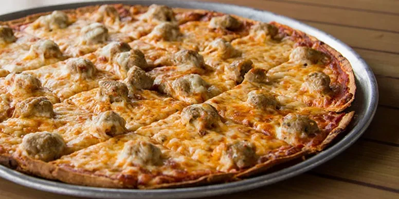 Sliced pizza with melted cheese and meat toppings on silver pan.
