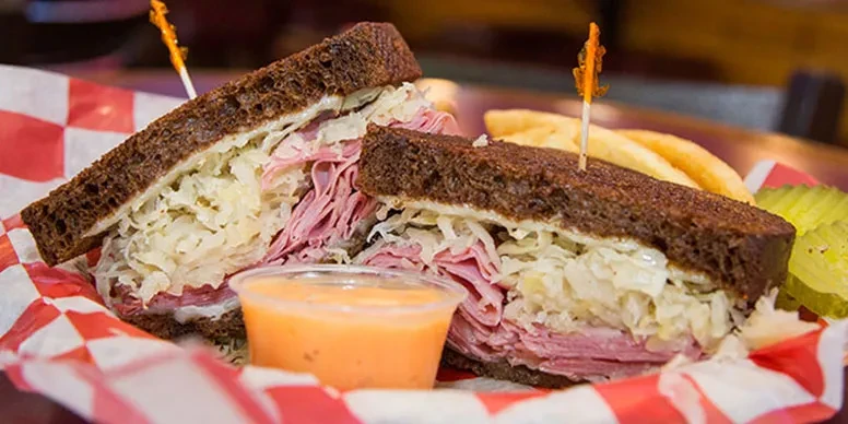 Deli meat sandwich, cut in half, with fries, pickle, and sauce.
