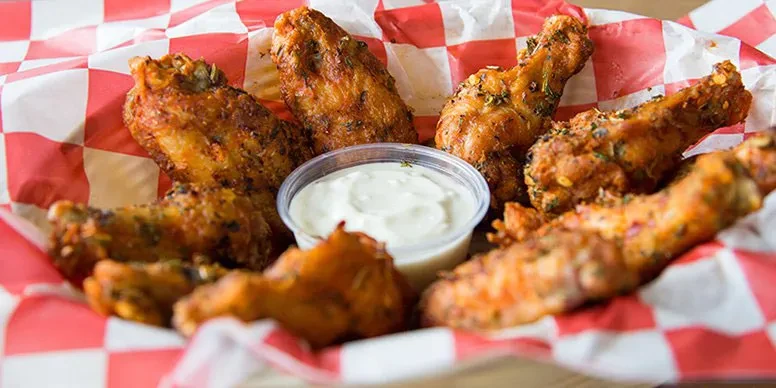 Seasoned fried chicken wings and creamy dipping sauce in a checkered basket.
