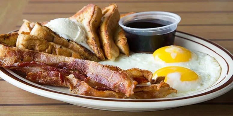 Hearty breakfast plate of French toast, bacon, eggs, cream, and syrup.