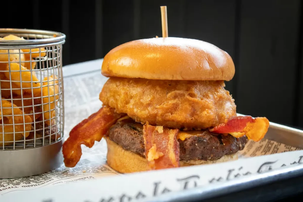 Stacked burger with bacon, onion ring, cheese, and golden fries.