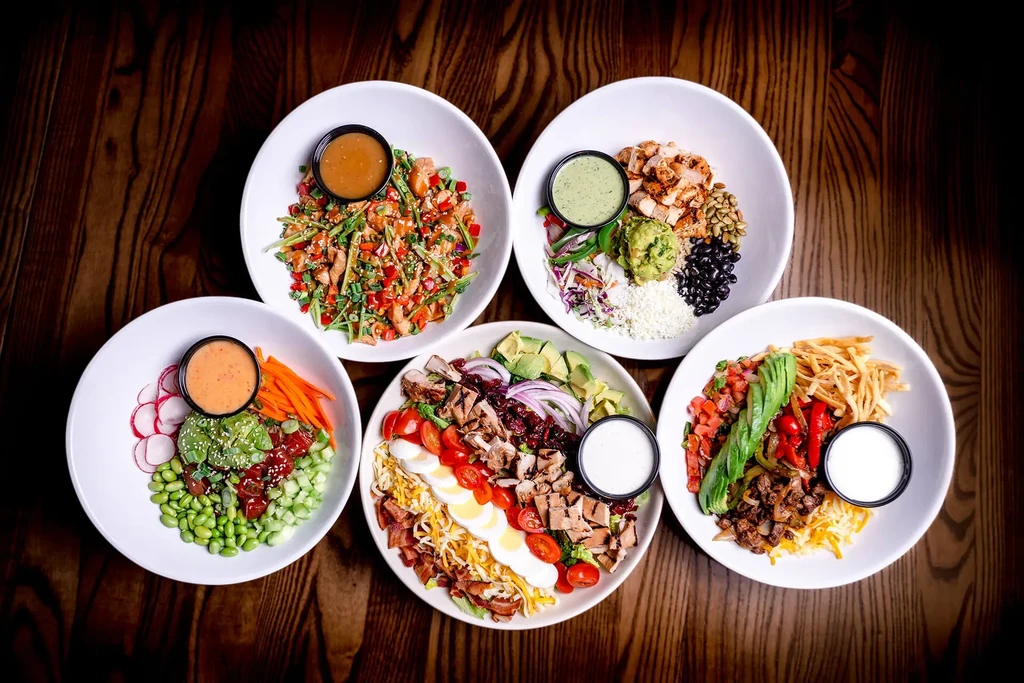 Five colorful grain and salad bowls on a brown wooden table.