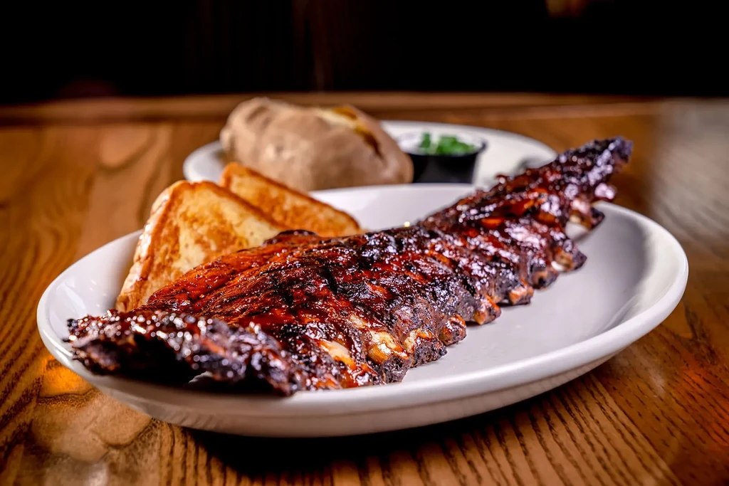 Glistening barbecue ribs, dark sauce, Texas toast, and baked potato.