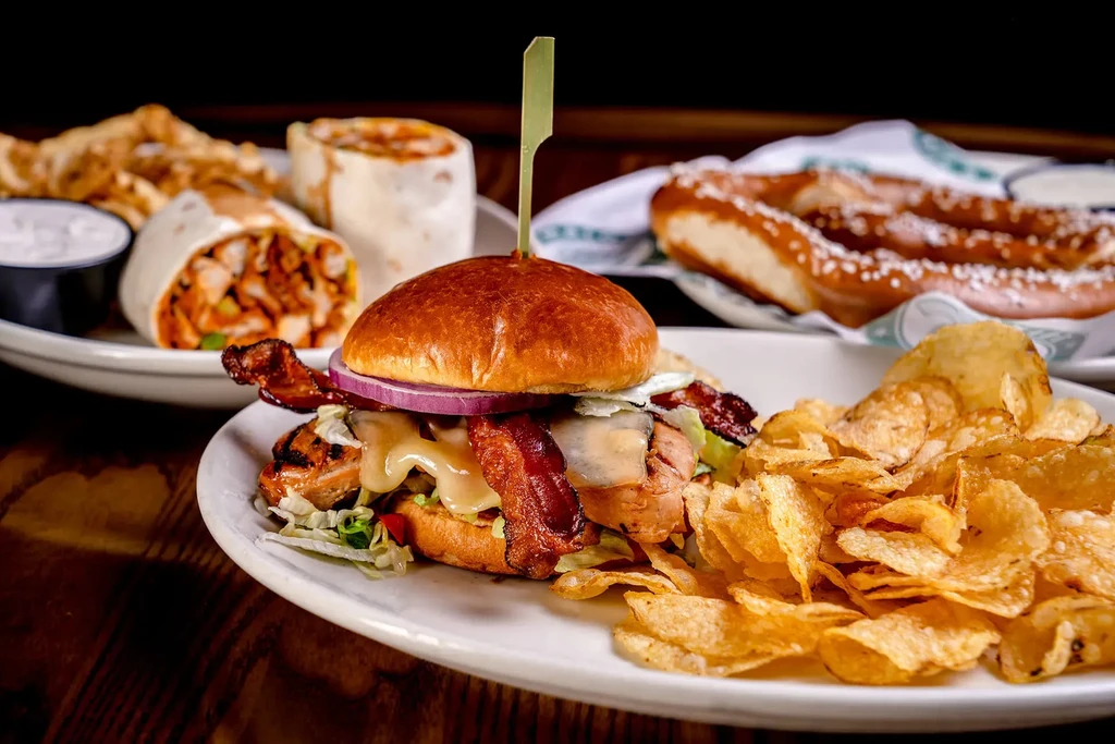Gourmet burger, chips, wrap halves, and pretzel on a rustic wooden table.