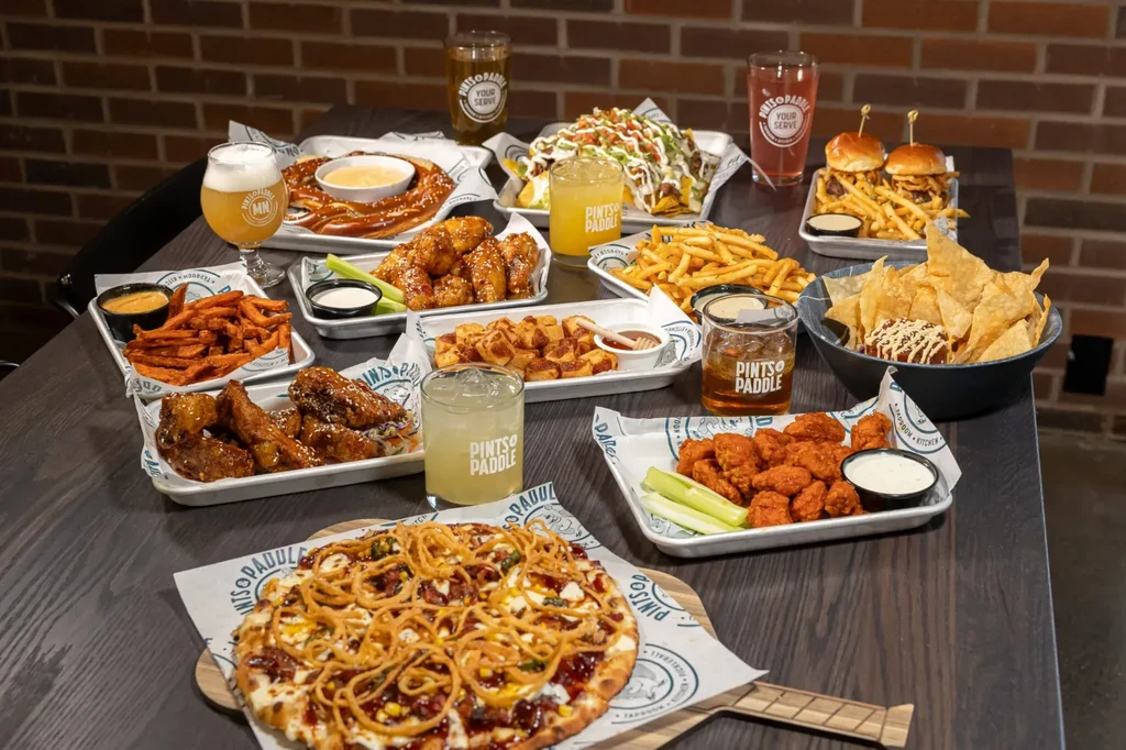 Diverse American pub food and Pints & Paddle branded drinks on a table.