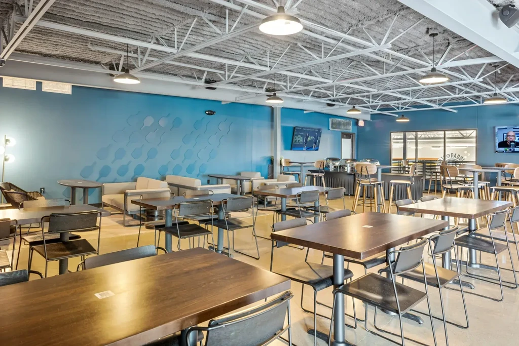 Empty modern restaurant with blue walls, exposed ceiling, and varied seating.