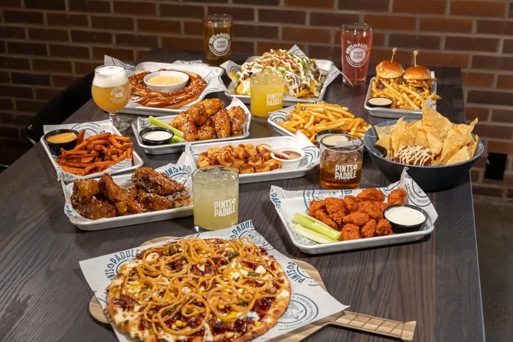 Overhead shot: pizza, wings, fries, nachos, and drinks on a table.